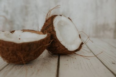 Tahta beyaz zeminde hindistan cevizi meyvesi. Bir hindistan cevizinin iki yarısı arka planda yatar. Seçili odak