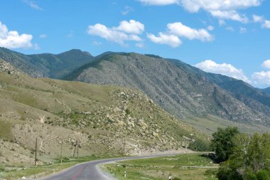 Dağların zirveleri gökyüzüne karşı beyaz bulutlarla. Yaz güneşli bir gün. Dağ asfalt yolu