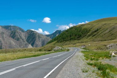 Dağların zirveleri gökyüzüne karşı beyaz bulutlarla. Yaz güneşli bir gün. Dağ asfalt yolu