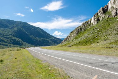 Dağların zirveleri gökyüzüne karşı beyaz bulutlarla. Yaz güneşli bir gün. Dağ asfalt yolu