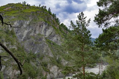 Geniş, huzursuz bir nehir, sularını dağ zirveleri arasında taşır. Yaz günü. Bulutlu hava.