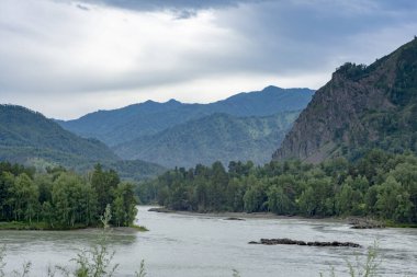 Geniş, huzursuz bir nehir, sularını dağ zirveleri arasında taşır. Yaz günü. Bulutlu hava.