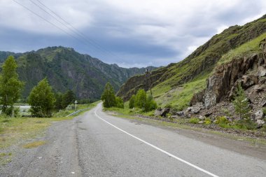 Dik dağ zirveleri arasındaki asfalt yol uzaklığa gider.