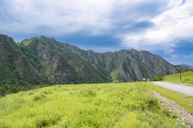 Dik dağ zirveleri arasındaki asfalt yol uzaklığa gider.