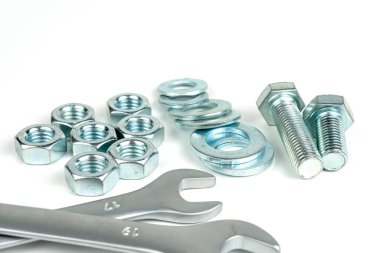 A small group of silver fasteners for fastening structures. Bolts and nuts with washers close-up on a white background. Several wrenches.