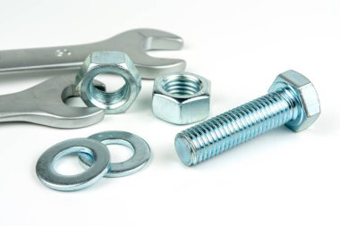 A small group of silver fasteners for fastening structures. Bolts and nuts with washers close-up on a white background. Several wrenches.