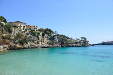 Porto Cristo 'daki sahil kayalıklarının tepesindeki evler. Sakin ol, turkuaz deniz suyu..