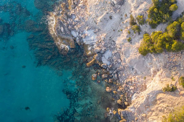 Aerial top down view of waves crashing against rocks in turquoise sea water