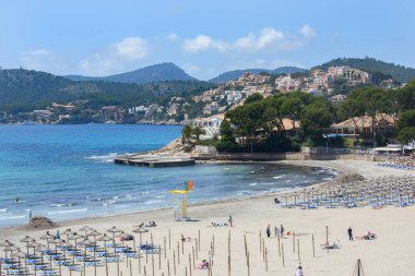 Peguera, Mallorca, İspanya - 05.01.2022: Peguera, Mallorca 'da sezon dışında plajdaki insanlar. Arka plandaki tepelerdeki evler.