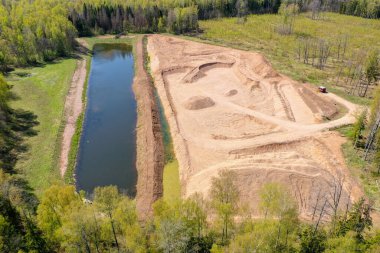 Açık kum, çakıl ocağı, su birikintisi ve ormanla çevrili havadan yüksek açı görüntüsü.
