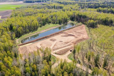 Açık kum, çakıl ocağı, su birikintisi ve ormanla çevrili havadan yüksek açı görüntüsü.