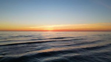 Aerial shot flying into beautiful orange sunset sky over waves in sea