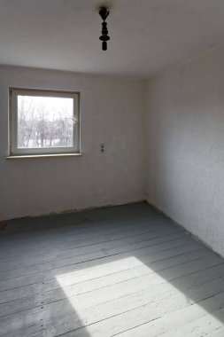 Gri döşemeleri ve beyaz duvarları olan küçük bir stüdyo ve parka bakan güney duvarında bir pencere..