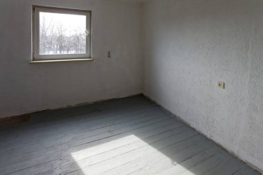 Gri döşemeleri ve beyaz duvarları olan küçük bir stüdyo ve parka bakan güney duvarında bir pencere..