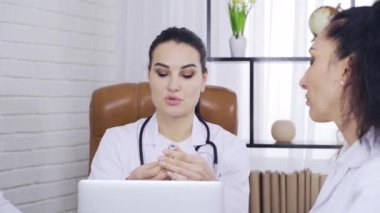 Doktor. Doğulu görünümlü bir kadın, doktor arkadaşlarına ilaç gösterir.