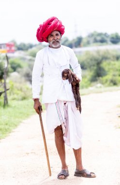 Jawai, Rajasthan, Hindistan - Eylül 2021: Jawai sahasında, ulusal başlık ve geleneksel beyaz elbise ve kırmızı sarıklı Rabari etnik grubunun yaşlı bir adamının portresi.