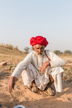 Puşkar, Rajasthan, Hindistan - Ekim 2017: Pushkar 'daki Deve Fuarında büyük bıyıklı Kırmızı Türbanlı Yaşlı Deve Taciri ve Beyaz Elbiseli