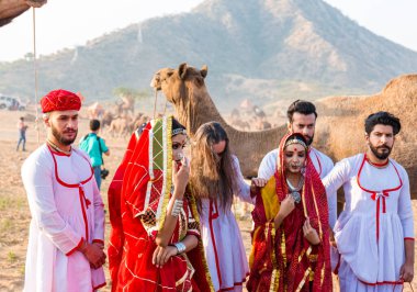 Puşkar, Rajasthan, Hindistan - Ekim 2019: Geleneksel Rajasthani ailesinin portre çekimi ve Pushkar Deve Fuarı 'nın arka planında develer