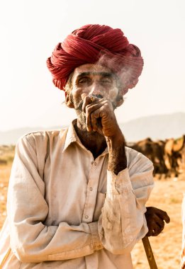 Puşkar, Rajasthan, Hindistan - Ekim 2017: Rajasthan 'lı Hintli adam fuar sırasında açık arazide sigara içiyor