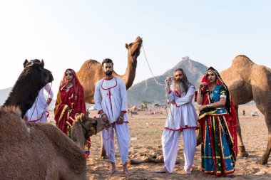 Puşkar, Rajasthan, Hindistan - Ekim 2019: Geleneksel Rajasthani ailesinin portre çekimi ve Pushkar Deve Fuarı 'nın arka planında develer