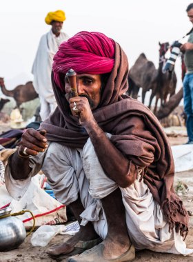 Puşkar, Rajasthan, Hindistan - Ekim 2017: Rajasthan 'lı Hintli adam fuar sırasında açık arazide sigara içiyor