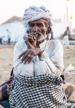 Puşkar, Rajasthan, Hindistan - Ekim 2017: Rajasthan 'lı Hintli adam fuar sırasında açık arazide sigara içiyor
