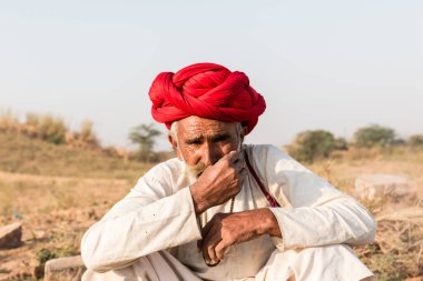 Puşkar, Rajasthan, Hindistan - Ekim 2017: Pushkar 'daki Deve Fuarında büyük bıyıklı Kırmızı Türbanlı Yaşlı Deve Taciri ve Beyaz Elbiseli
