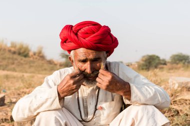 Puşkar, Rajasthan, Hindistan - Ekim 2017: Pushkar 'daki Deve Fuarında büyük bıyıklı Kırmızı Türbanlı Yaşlı Deve Taciri ve Beyaz Elbiseli