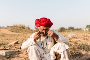 Puşkar, Rajasthan, Hindistan - Ekim 2017: Pushkar 'daki Deve Fuarında büyük bıyıklı Kırmızı Türbanlı Yaşlı Deve Taciri ve Beyaz Elbiseli