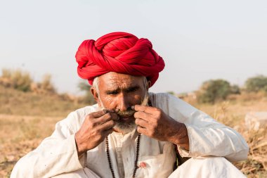 Puşkar, Rajasthan, Hindistan - Ekim 2017: Pushkar 'daki Deve Fuarında büyük bıyıklı Kırmızı Türbanlı Yaşlı Deve Taciri ve Beyaz Elbiseli