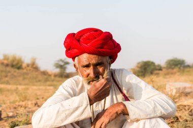 Puşkar, Rajasthan, Hindistan - Ekim 2017: Pushkar 'daki Deve Fuarında büyük bıyıklı Kırmızı Türbanlı Yaşlı Deve Taciri ve Beyaz Elbiseli