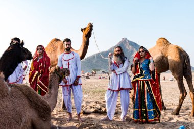 Puşkar, Rajasthan, Hindistan - Ekim 2019: Geleneksel Rajasthani ailesinin portre çekimi ve Pushkar Deve Fuarı 'nın arka planında develer