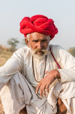 Puşkar, Rajasthan, Hindistan - Ekim 2017: Pushkar 'daki Deve Fuarında büyük bıyıklı Kırmızı Türbanlı Yaşlı Deve Taciri ve Beyaz Elbiseli
