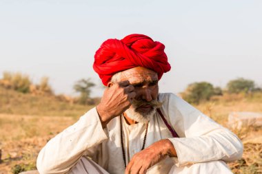 Puşkar, Rajasthan, Hindistan - Ekim 2017: Pushkar 'daki Deve Fuarında büyük bıyıklı Kırmızı Türbanlı Yaşlı Deve Taciri ve Beyaz Elbiseli