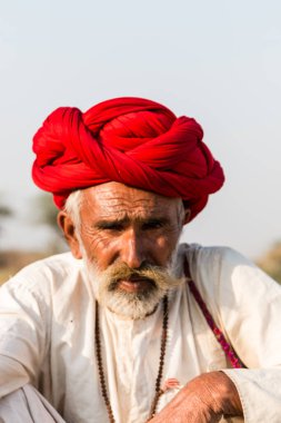 Puşkar, Rajasthan, Hindistan - Ekim 2017: Pushkar 'daki Deve Fuarında büyük bıyıklı Kırmızı Türbanlı Yaşlı Deve Taciri ve Beyaz Elbiseli