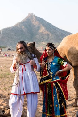 Puşkar, Rajasthan, Hindistan - Ekim 2019: Geleneksel Rajasthani ailesinin portre çekimi ve Pushkar Deve Fuarı 'nın arka planında develer