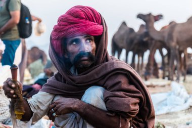 Puşkar, Rajasthan, Hindistan - Ekim 2017: Rajasthan 'lı Hintli adam fuar sırasında açık arazide sigara içiyor