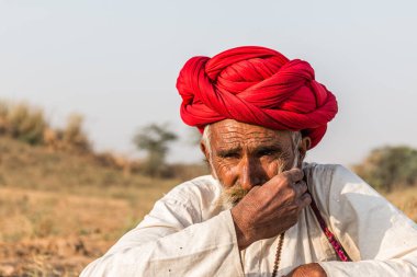 Puşkar, Rajasthan, Hindistan - Ekim 2017: Pushkar 'daki Deve Fuarında büyük bıyıklı Kırmızı Türbanlı Yaşlı Deve Taciri ve Beyaz Elbiseli