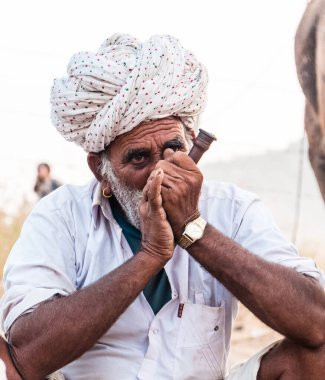 Puşkar, Rajasthan, Hindistan - Ekim 2017: Rajasthan 'lı Hintli adam fuar sırasında açık arazide sigara içiyor