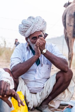 Puşkar, Rajasthan, Hindistan - Ekim 2017: Rajasthan 'lı Hintli adam fuar sırasında açık arazide sigara içiyor