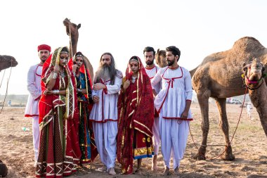 Puşkar, Rajasthan, Hindistan - Ekim 2019: Geleneksel Rajasthani ailesinin portre çekimi ve Pushkar Deve Fuarı 'nın arka planında develer