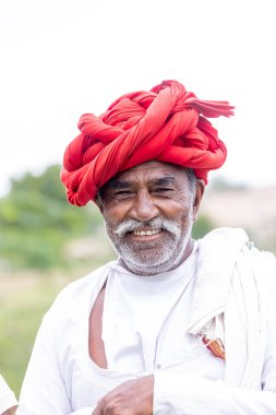 Jawai, Rajasthan, Hindistan - Eylül 2021: Jawai sahasında, ulusal başlık ve geleneksel beyaz elbise ve kırmızı sarıklı Rabari etnik grubunun yaşlı bir adamının portresi.