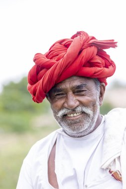 Jawai, Rajasthan, Hindistan - Eylül 2021: Jawai sahasında, ulusal başlık ve geleneksel beyaz elbise ve kırmızı sarıklı Rabari etnik grubunun yaşlı bir adamının portresi.