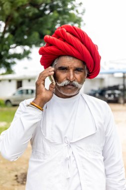 Jawai, Rajasthan, Hindistan - Eylül 2021: Jawai sahasında, ulusal başlık ve geleneksel beyaz elbise ve kırmızı sarıklı Rabari etnik grubunun yaşlı bir adamının portresi.