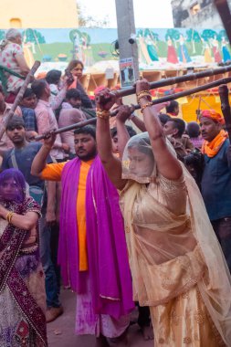 Barsana, Uttar Pradesh, Hindistan - Mart 2022: Barsana 'lı Hindu kadınlar ellerinde peçeleri ve bambu çubuklarıyla erkek insanları Nandgaon' dan geleneksel lathmar holi ritüeli olarak yeniyorlar.