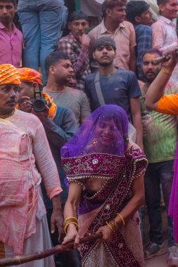 Barsana, Uttar Pradesh, Hindistan - Mart 2022: Barsana 'lı Hindu kadınlar ellerinde peçeleri ve bambu çubuklarıyla erkek insanları Nandgaon' dan geleneksel lathmar holi ritüeli olarak yeniyorlar.
