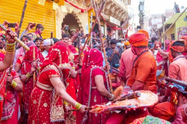 Barsana, Uttar Pradesh, Hindistan - Mart 2022: Barsana 'lı Hindu kadınlar ellerinde peçeleri ve bambu çubuklarıyla erkek insanları Nandgaon' dan geleneksel lathmar holi ritüeli olarak yeniyorlar.