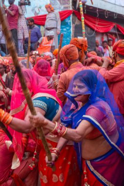 Barsana, Uttar Pradesh, Hindistan - Mart 2022: Barsana 'lı Hindu kadınlar ellerinde peçeleri ve bambu çubuklarıyla erkek insanları Nandgaon' dan geleneksel lathmar holi ritüeli olarak yeniyorlar.