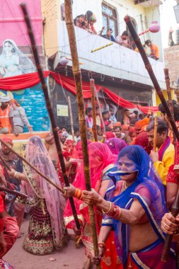 Barsana, Uttar Pradesh, Hindistan - Mart 2022: Barsana 'lı Hindu kadınlar ellerinde peçeleri ve bambu çubuklarıyla erkek insanları Nandgaon' dan geleneksel lathmar holi ritüeli olarak yeniyorlar.