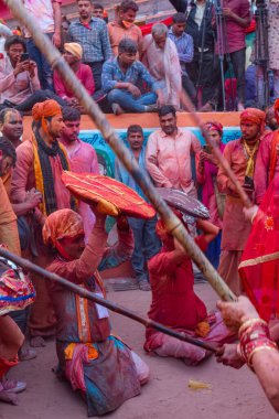 Barsana, Uttar Pradesh, Hindistan - Mart 2022: Barsana 'lı Hindu kadınlar ellerinde peçeleri ve bambu çubuklarıyla erkek insanları Nandgaon' dan geleneksel lathmar holi ritüeli olarak yeniyorlar.